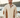 Man wearing a beige pullover with tan suede accents and button-up collar, styled with jeans on a coastal patio – modern Australian men’s smart-casual fashion by Beige Rue.